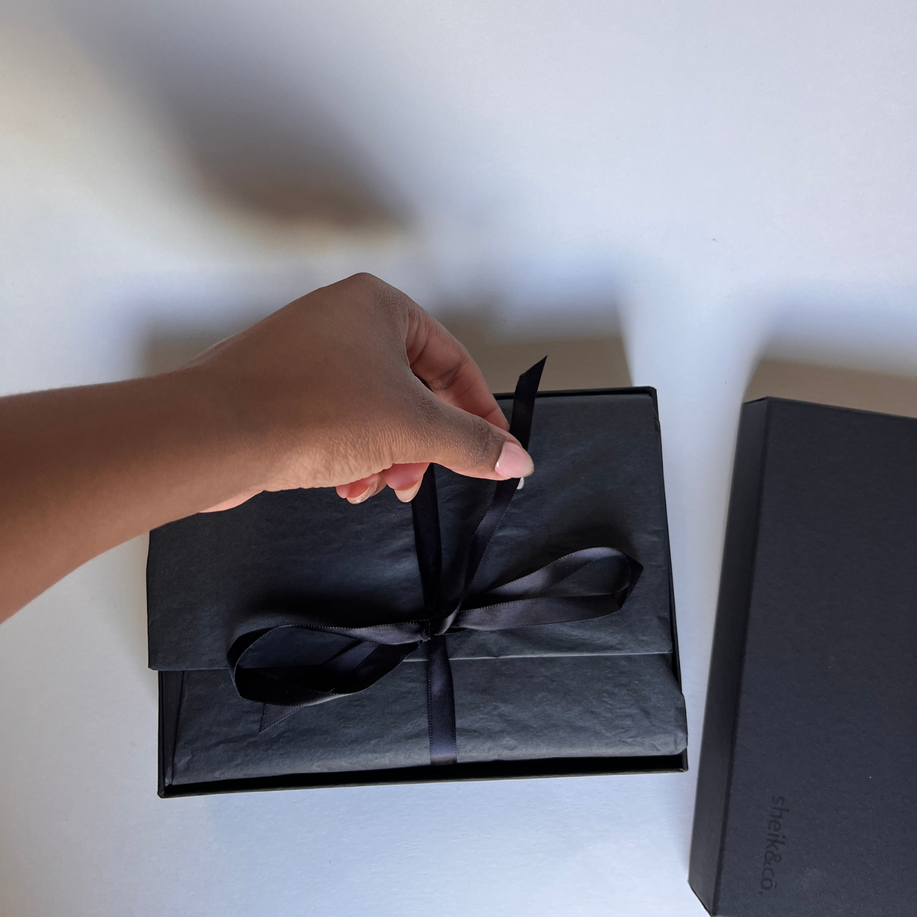 Hand opening a black gift box with a ribbon on a white surface